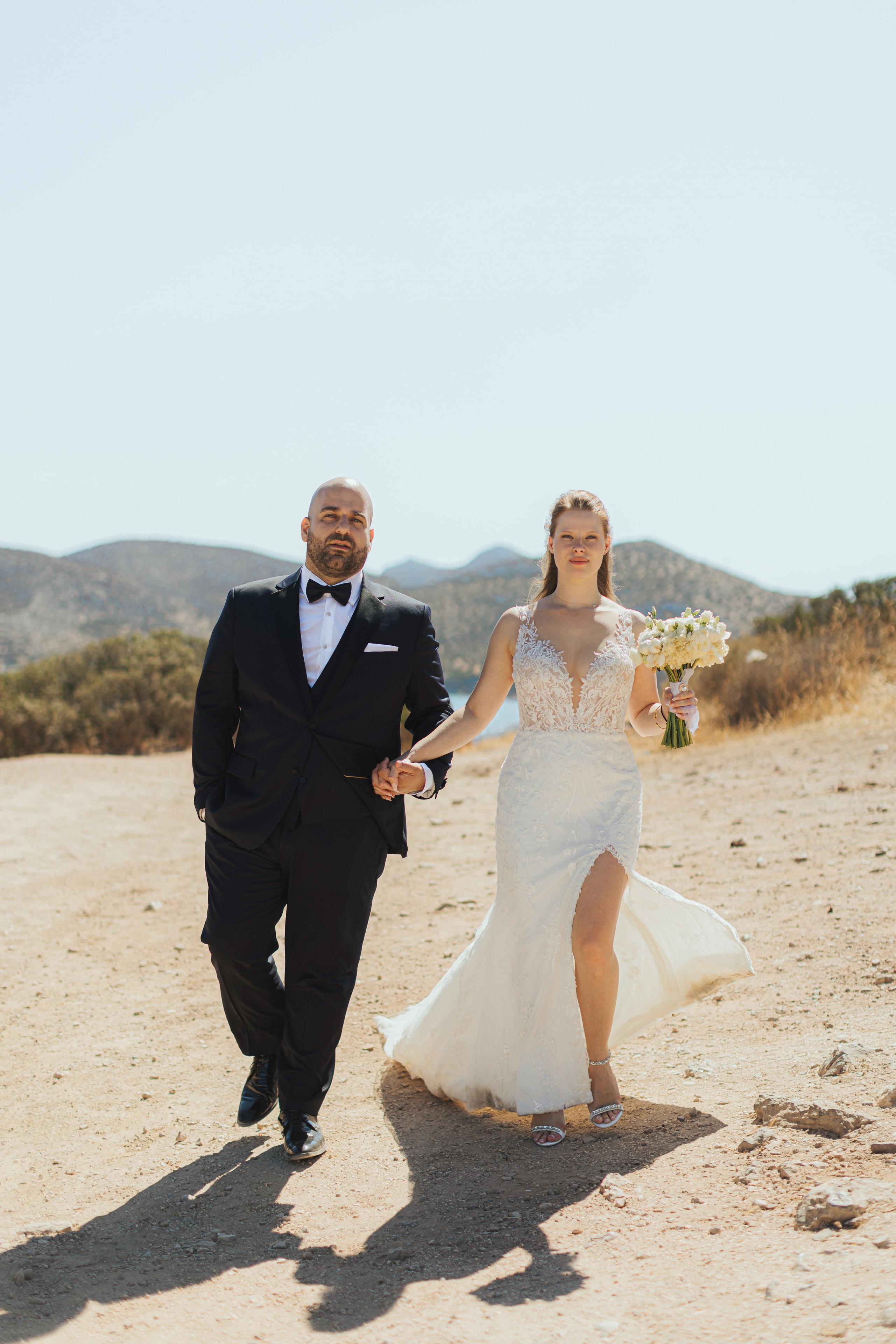 Agis and Ioanna walking together through a sunlit coastal landscape