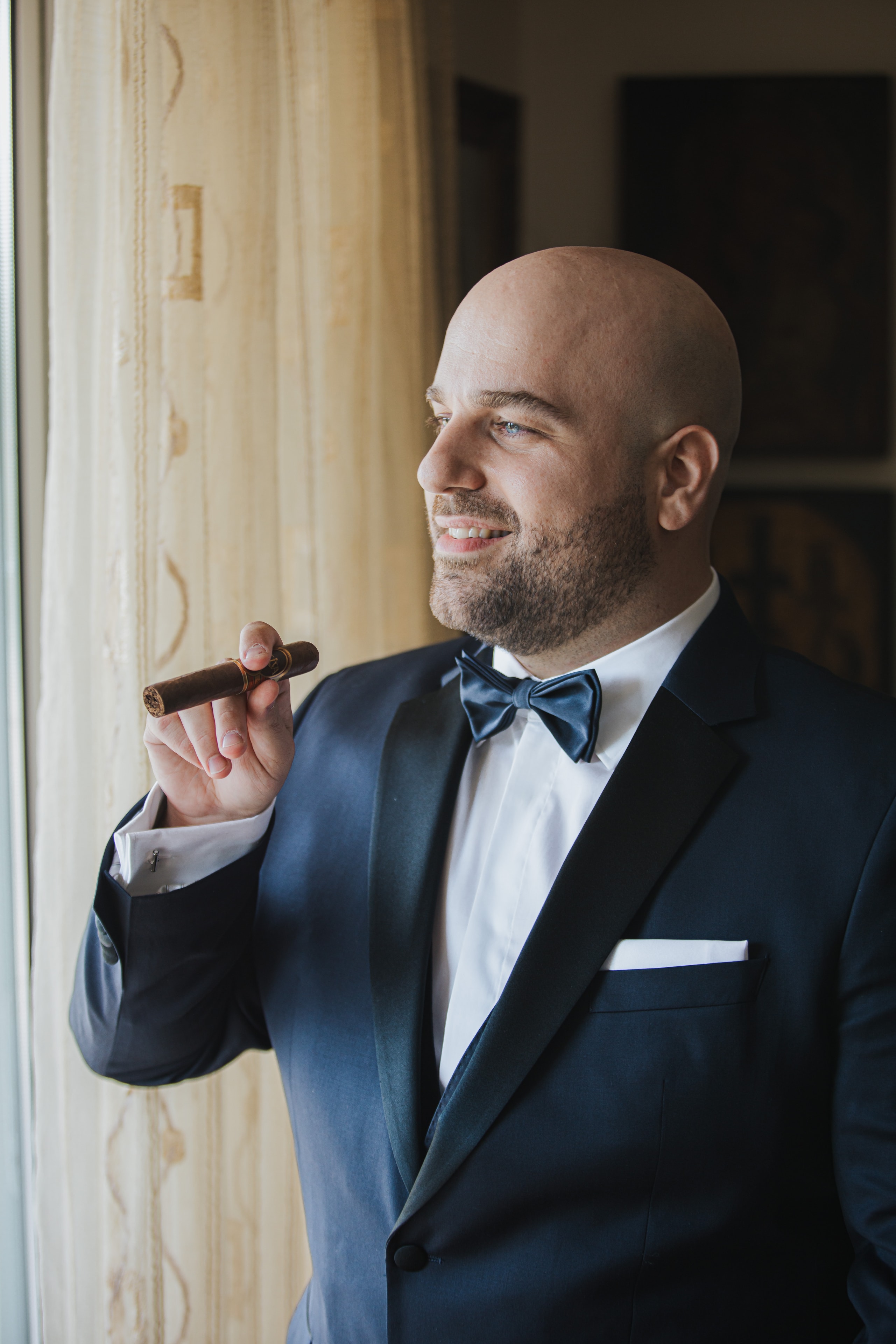 Agis in a tuxedo holding a cigar by the window