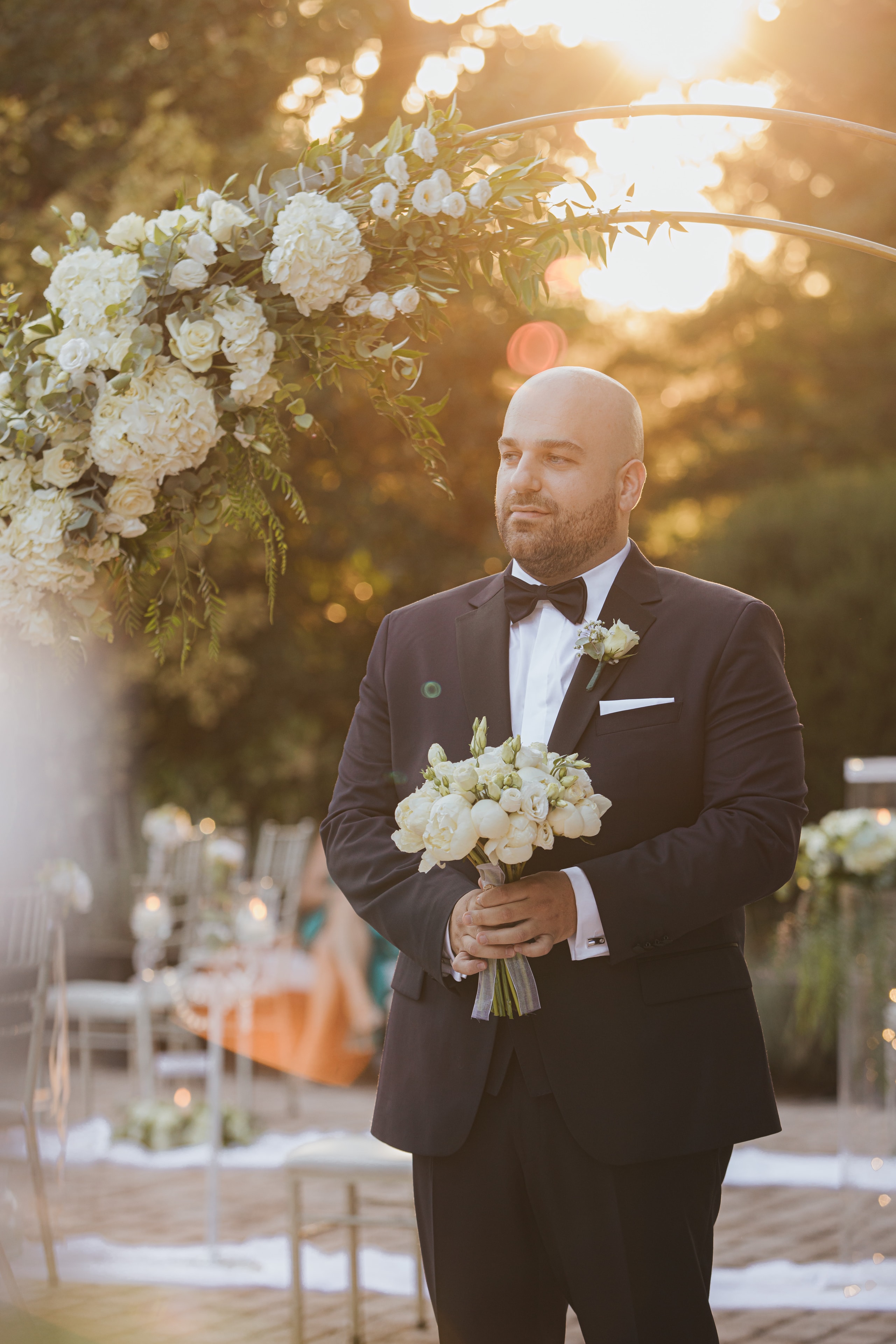 Agis holding a white bouquet beneath the floral arch