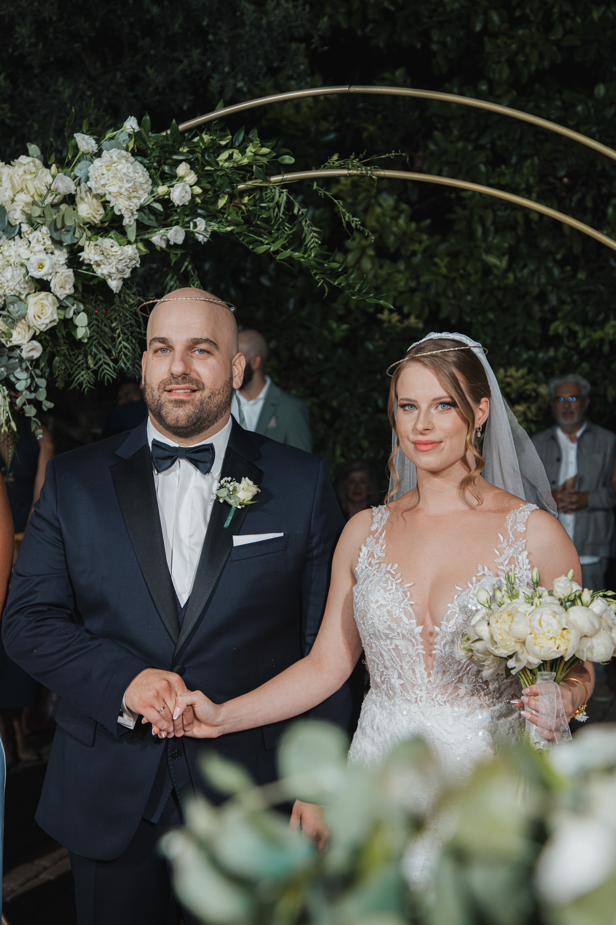 Agis and Ioanna beneath their floral ceremony arch