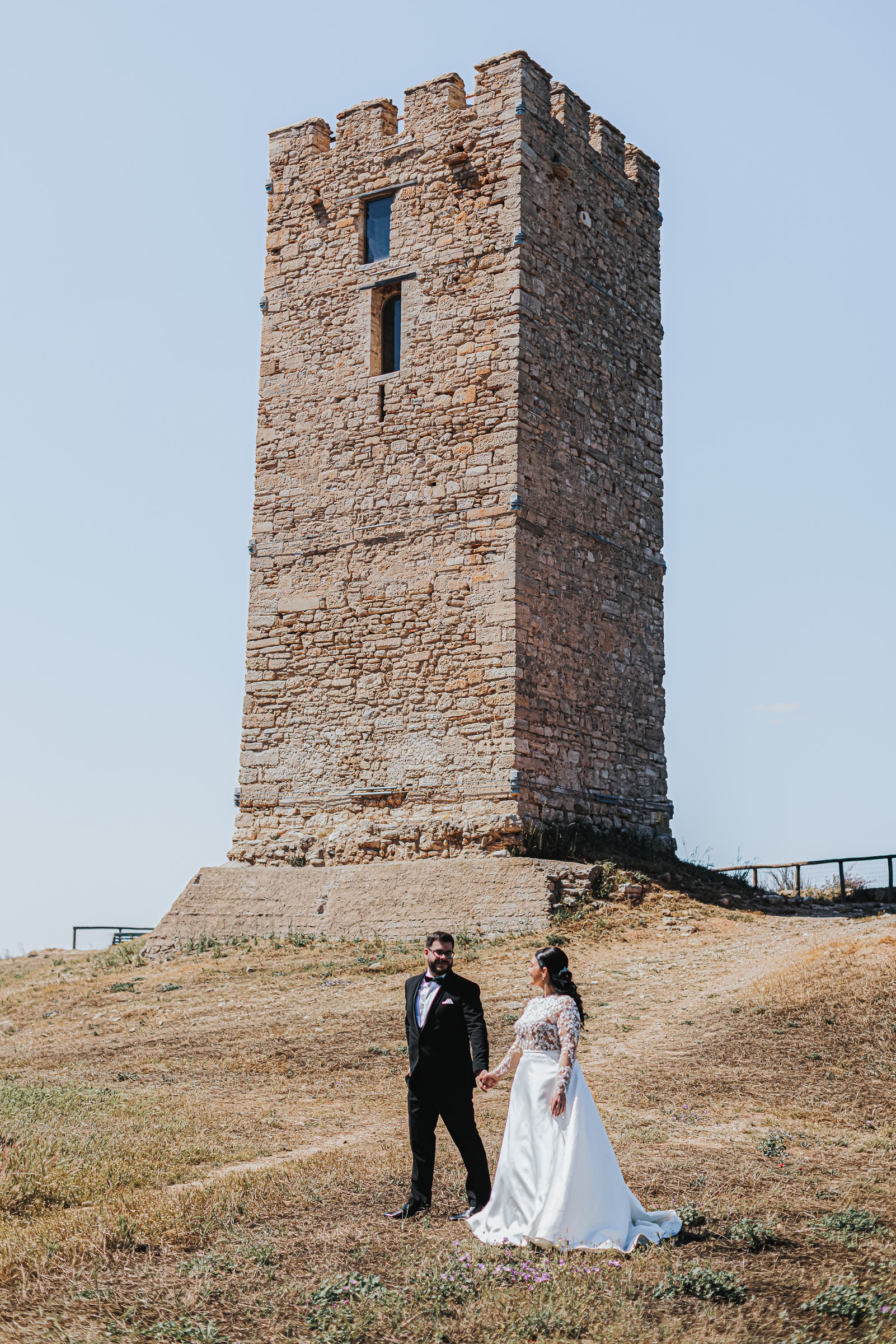 Ioanna and Christos beside a historic stone tower