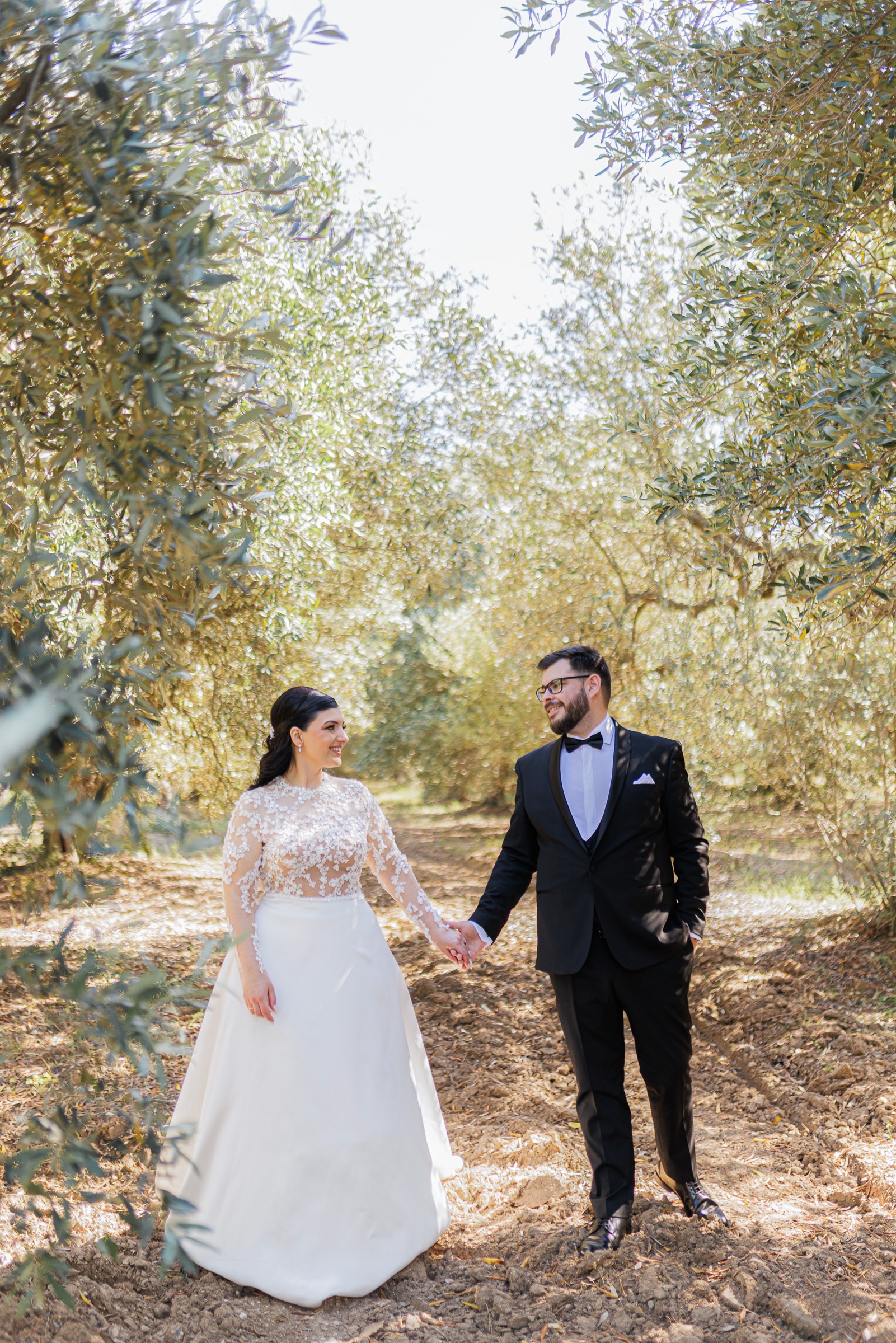 Ioanna and Christos walking hand in hand through an olive grove
